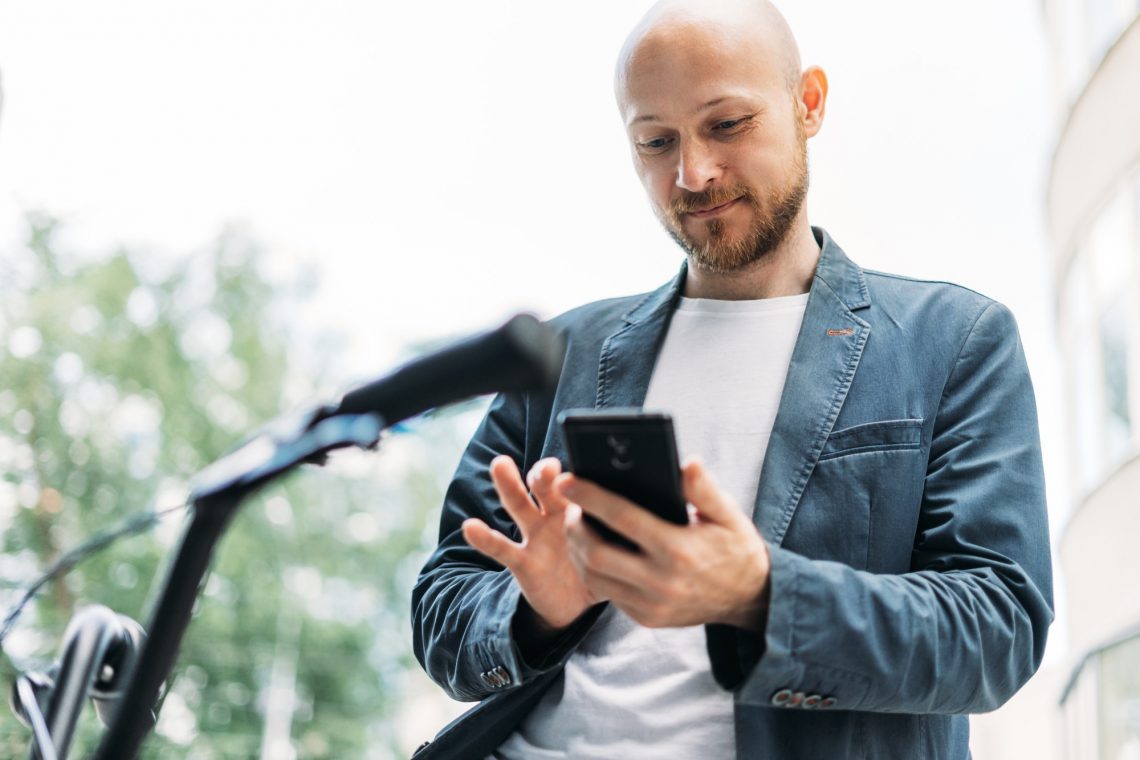 Adult bald bearded man in blue suit with mobile on bicycle